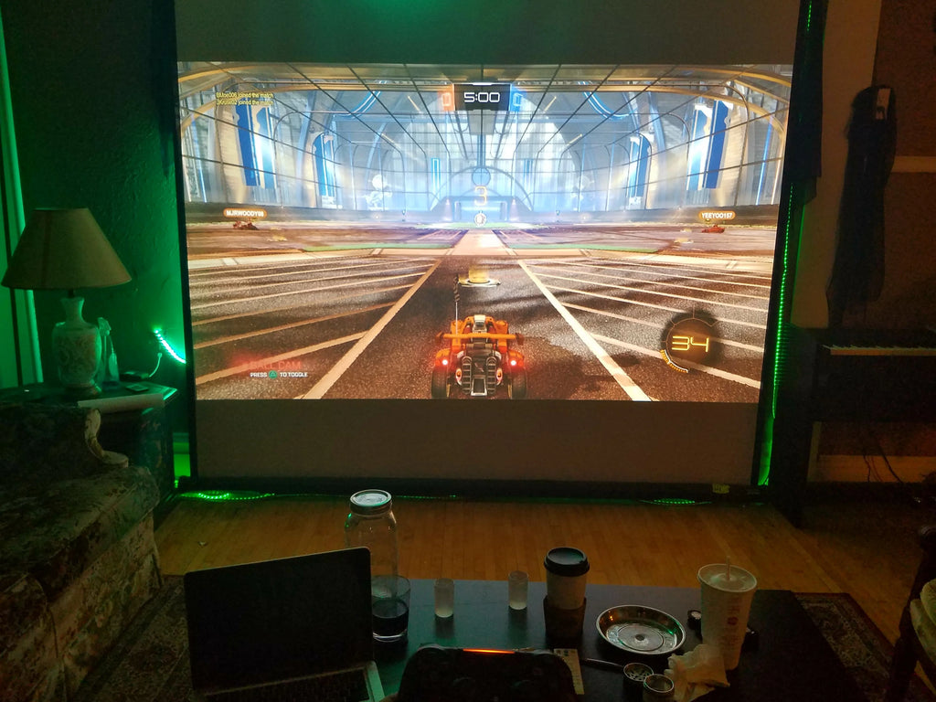 HighPeak MiniProjector projecting a vivid game screen onto a large wall in a cozy living room at night