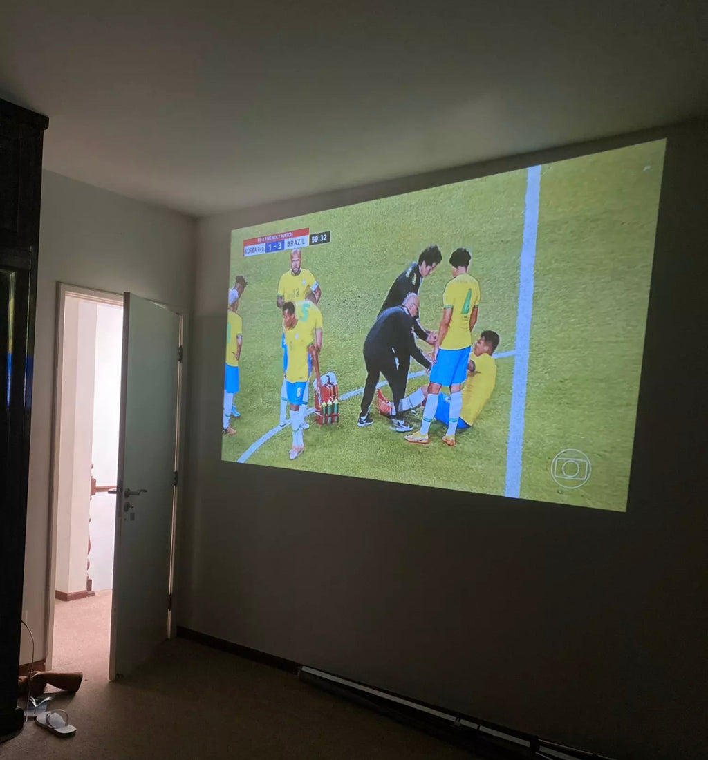 HighPeak MiniProjector™ projecting a soccer game on a plain white wall in a dimly lit room.