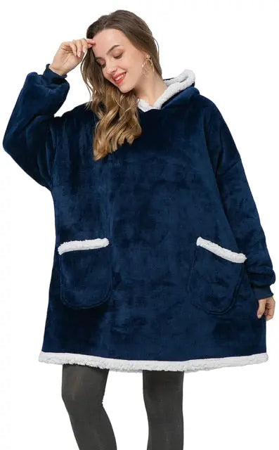 Oversized Hoodie Blanket in navy blue with sherpa lining and front pockets, shown worn as cozy winter loungewear