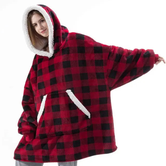 Oversized Hoodie Blanket in red and black buffalo plaid with sherpa-lined hood and kangaroo pocket, worn in cozy indoor setting