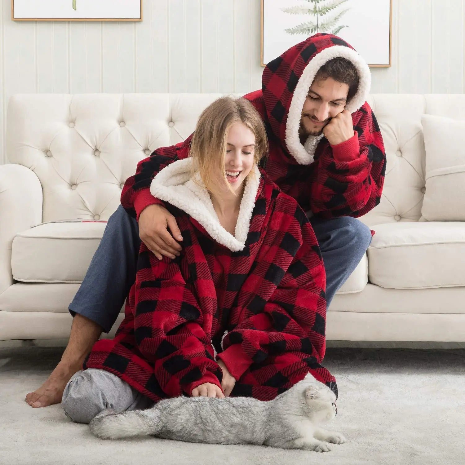Oversized Hoodie Blanket in red buffalo plaid with sherpa lining, shown on couple relaxing on white couch with cat