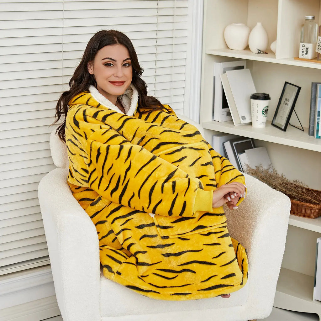 Oversized Hoodie Blanket in yellow tiger stripe pattern worn by person relaxing in white armchair, cozy home setting