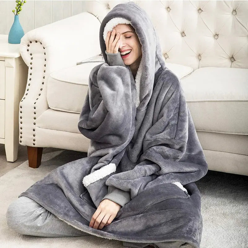 Person wearing grey Oversized Hoodie Blanket lounging on white couch, showcasing plush sherpa-lined comfort and roomy design